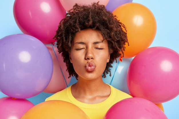 Colpo del primo piano di bella giovane donna in posa circondata da palloncini colorati compleanno