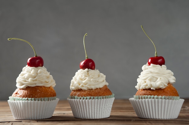 Colpo del primo piano di deliziosi cupcakes con panna e ciliegie in cima