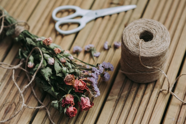 Colpo del primo piano di spago con le forbici bianche e fiori secchi su una superficie di legno