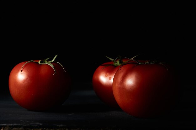 Colpo del primo piano di tre pomodori freschi su sfondo nero