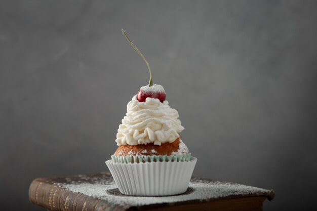 Colpo del primo piano di un delizioso cupcake con panna, zucchero a velo e una ciliegina sulla torta su un libro