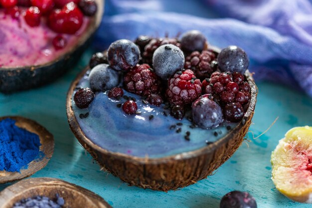 Colpo del primo piano di un frullato di frutta condito con lamponi e mirtilli congelati in un piatto di cocco