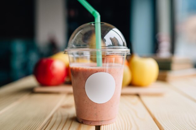 Colpo del primo piano di un frullato in una tazza da asporto con frutta fresca sullo sfondo