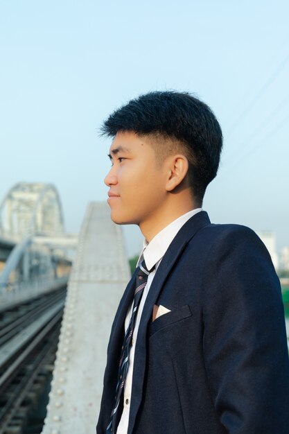 Colpo del primo piano di un giovane uomo asiatico in un vestito in piedi su un ponte e guardando lontano
