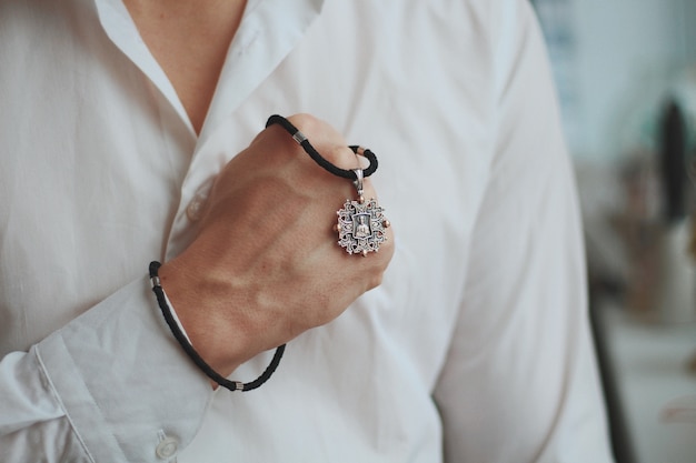 Colpo del primo piano di un maschio che tiene una collana di fascino con un ciondolo d'argento e un cavo nero