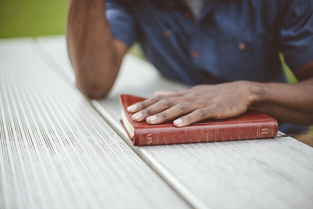 Colpo del primo piano di un maschio con la sua mano sulla bibbia su una tavola di legno