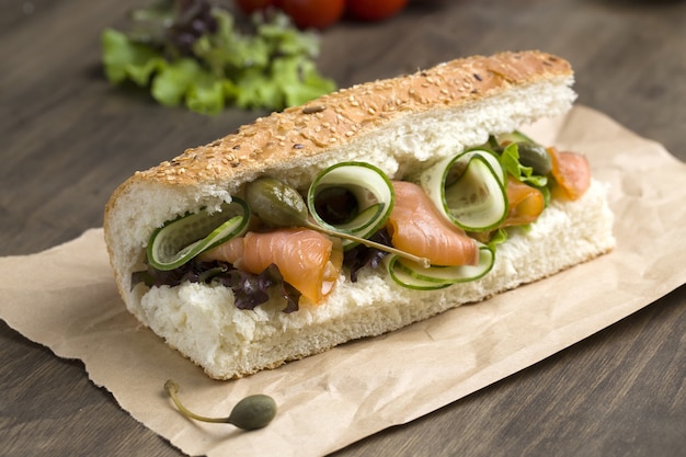 Colpo del primo piano di un panino al salmone con verdure fresche in un pane baguette