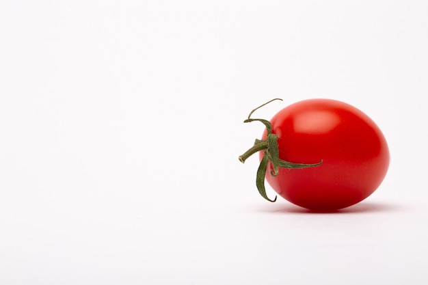 Colpo del primo piano di un pomodoro ciliegia su una parete bianca - perfetto per un blog dell'alimento