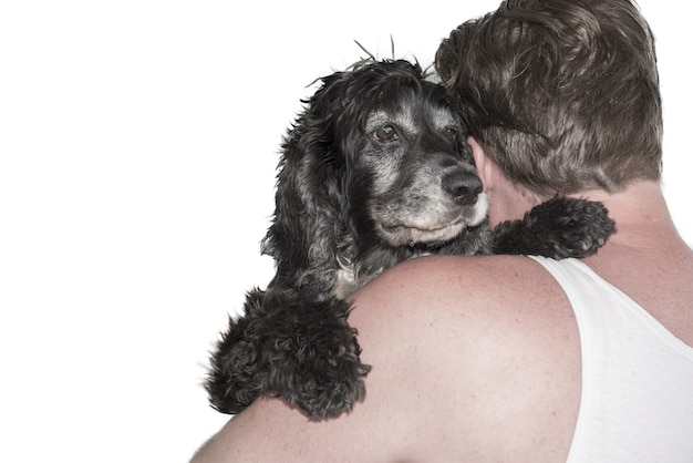 Colpo del primo piano di un uomo che abbraccia un cane nero dietro su bianco