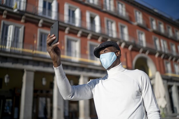 Colpo del primo piano di un uomo di colore che tiene il suo telefono che indossa un concetto a collo alto della nuova normalità