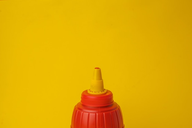 Colpo del primo piano di una bottiglia di ketchup rossa su una parete gialla