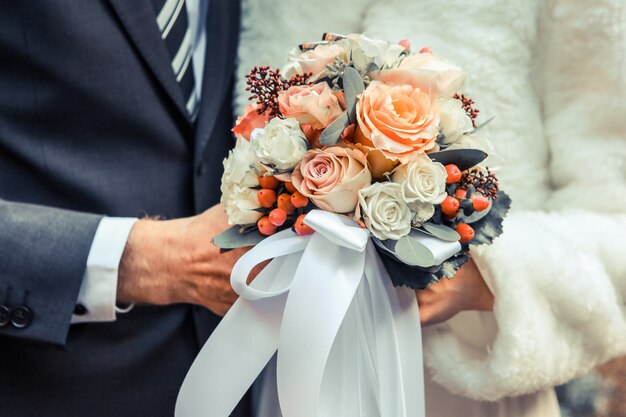 Colpo del primo piano di una coppia di sposi in possesso di un bouquet di fiori con rose bianche e arancioni