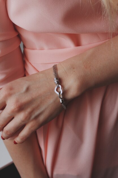 Colpo del primo piano di una donna in un abito rosa che indossa un bellissimo braccialetto d'argento con un ciondolo a cuore