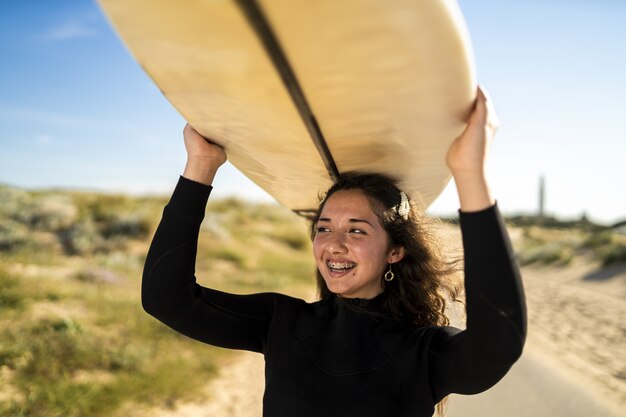 Colpo del primo piano di una donna sorridente che porta una tavola da surf sopra la sua testa