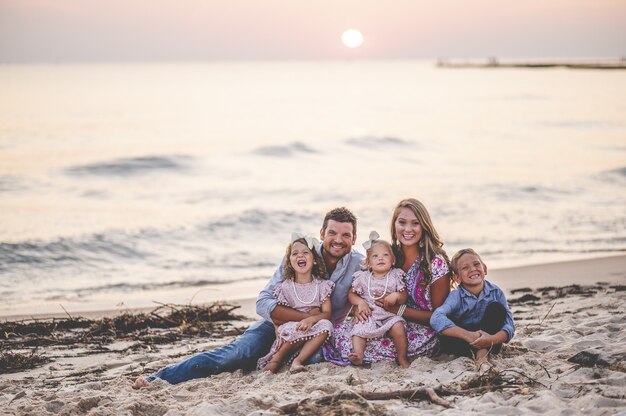 Colpo del primo piano di una famiglia felice che si siede in riva al mare al tramonto - concetto di famiglia