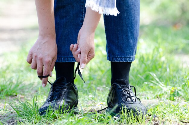 Colpo del primo piano di una femmina che lega i suoi lacci delle scarpe su un sentiero con erba