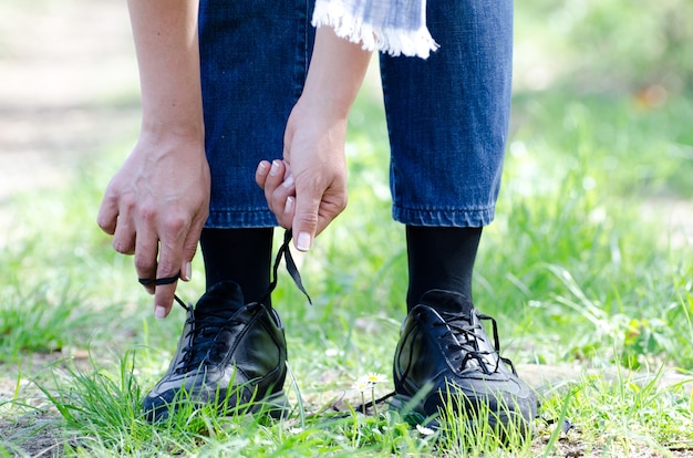 Colpo del primo piano di una femmina che lega i suoi lacci delle scarpe su un sentiero con erba