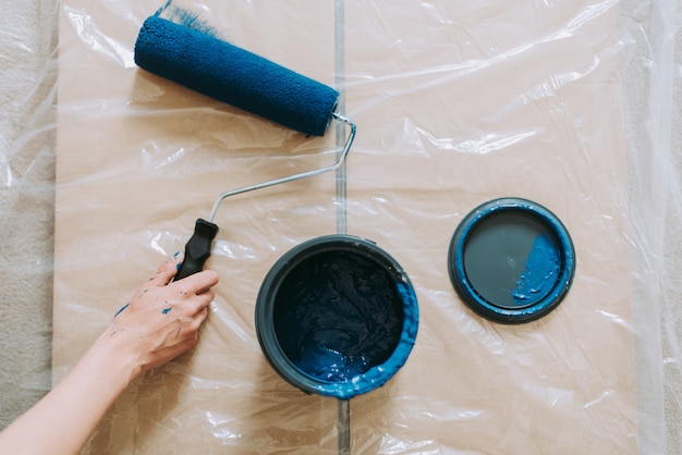 Colpo del primo piano di una femmina che usando i rulli di pittura con il blu di colore