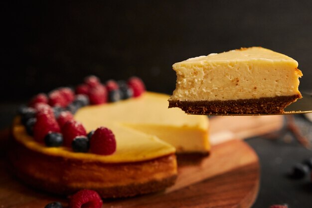 Colpo del primo piano di una fetta di torta di formaggio con la torta con frutti di bosco in cima