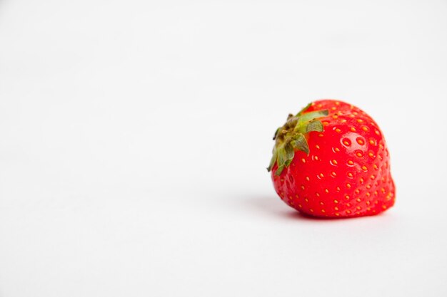 Colpo del primo piano di una fragola rossa su una superficie bianca