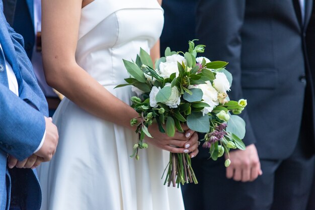 Colpo del primo piano di una sposa che tiene il suo bellissimo bouquet in piedi presso l'altare