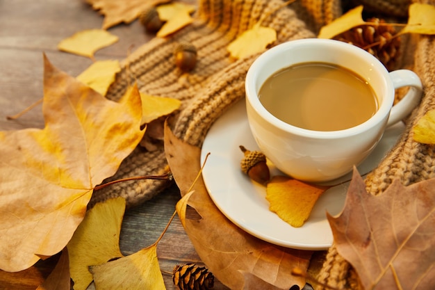 Colpo del primo piano di una tazza di caffè e foglie di autunno su una superficie di legno