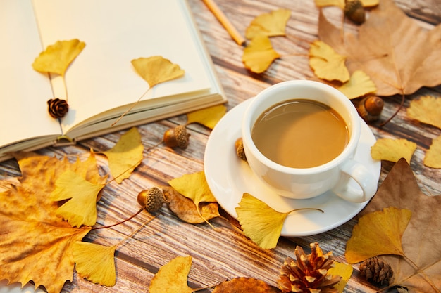 Colpo del primo piano di una tazza di caffè e foglie di autunno su una superficie di legno