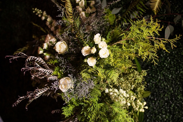 Colpo di alto angolo di un bouquet con foglie sempreverdi e rose bianche sotto le luci