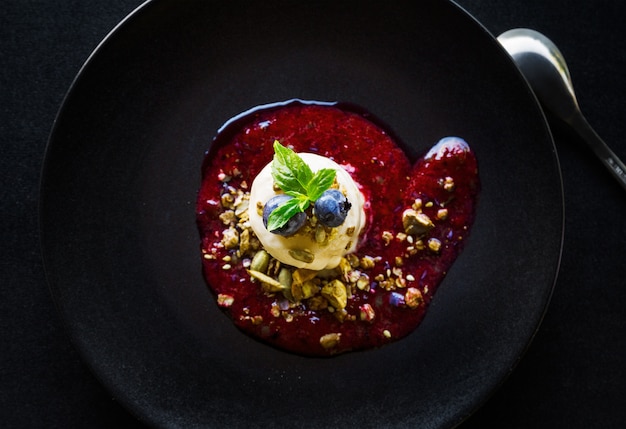 Colpo di alto angolo di un delizioso dessert rosso con crema bianca, bacche e noci in una ciotola nera