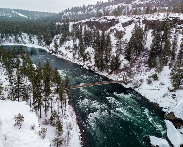 Colpo di alto angolo di un fiume in mezzo a montagne innevate coperte di alberi