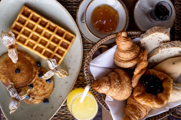 Colpo di alto angolo di un pancake e waffle in un piatto rotondo vicino al trey con cornetto