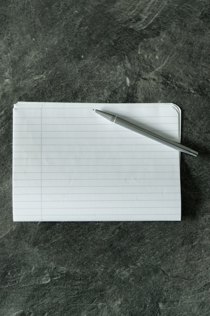 Colpo di alto angolo di un pezzo di carta bianca con linee e una penna di metallo su una superficie grigia