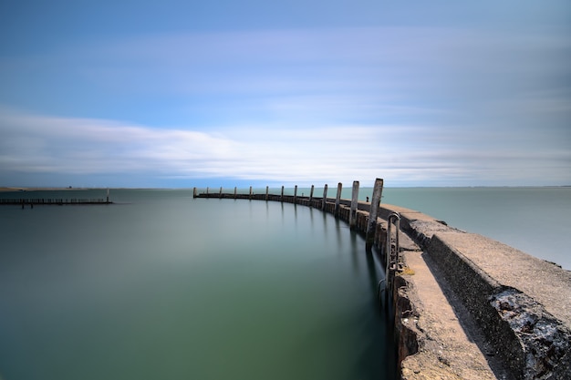 Colpo di alto angolo di un ponte di legno che conduce al mare sotto un cielo blu chiaro
