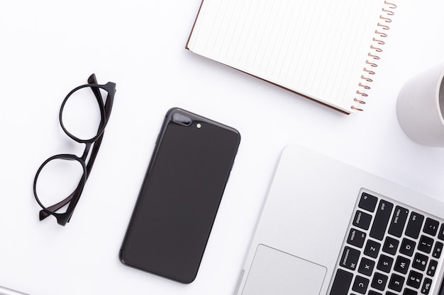 Colpo di alto angolo di uno smartphone, laptop, occhiali e un notebook su una superficie bianca
