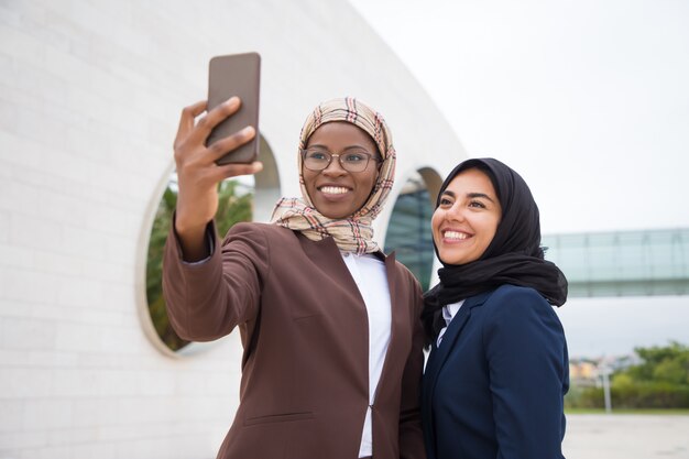 Colpo di angolo basso delle donne di affari musulmane sorridenti che prendono selfie