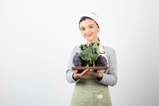 Colpo di cuoco sorridente che tiene piatto di cavolo e broccoli su bianco