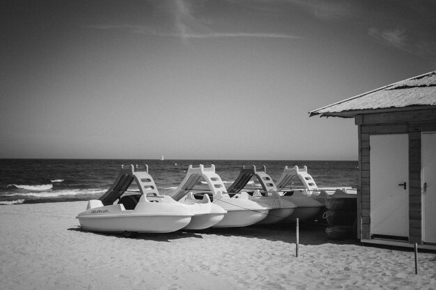 Colpo di gradazione di grigio di natanti o imbarcazioni marine vicino a una cabina su una spiaggia sabbiosa