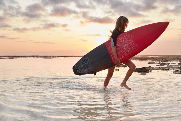 Colpo di istruttore di surf esperto trasporta la tavola da surf, cavalca le onde sull'oceano, va a riva dall'acqua, si prepara per la gara