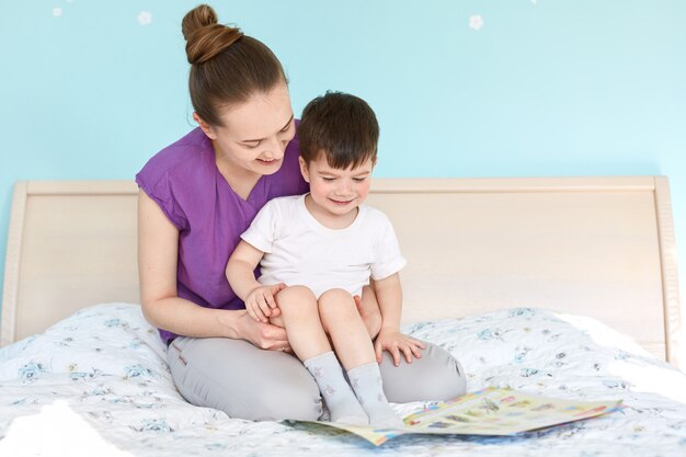 Colpo di madre premurosa in congedo di maternità e bambino piccolo leggere la fiaba prima di dormire