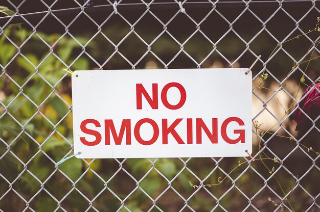 Colpo di messa a fuoco del primo piano del segno "vietato fumare" appeso alla recinzione