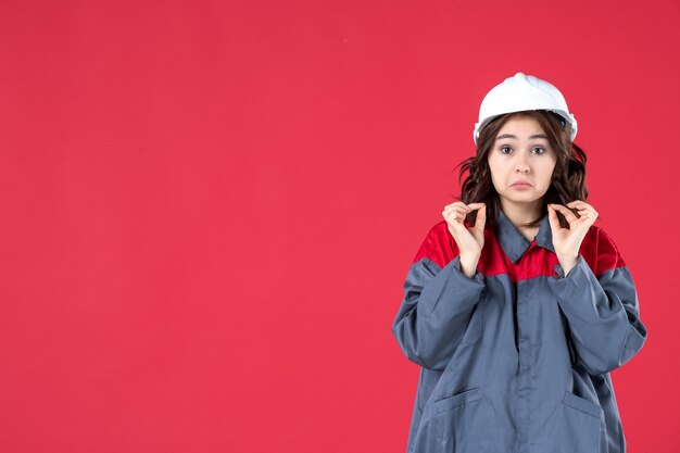 Colpo di mezzo corpo di infelice costruttore femminile in uniforme con elmetto su sfondo rosso isolato