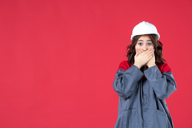 Colpo di mezzo corpo di una donna impaurita in uniforme con elmetto su sfondo rosso isolato