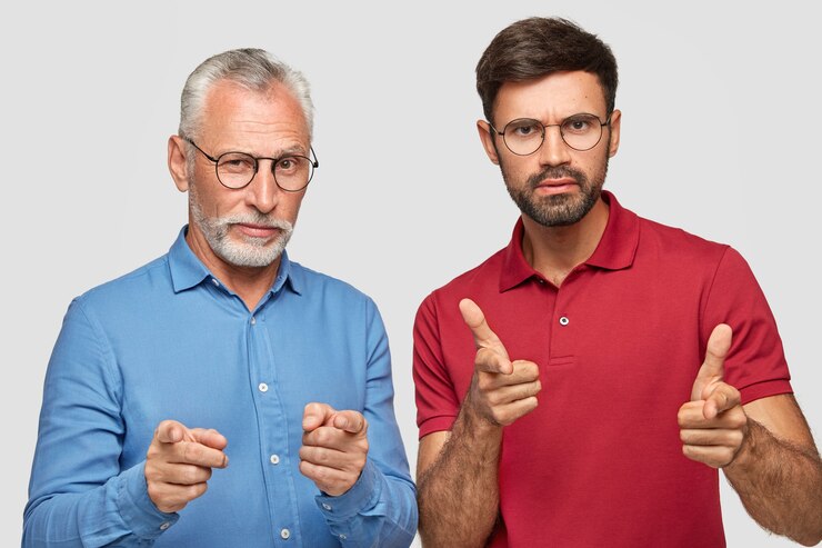 Foto gratuito colpo di partner maschi seri e sicuri di sé di diversa età direttamente, fare la scelta, indossare una camicia blu formale e una maglietta rossa brillante, posare insieme contro il muro bianco.