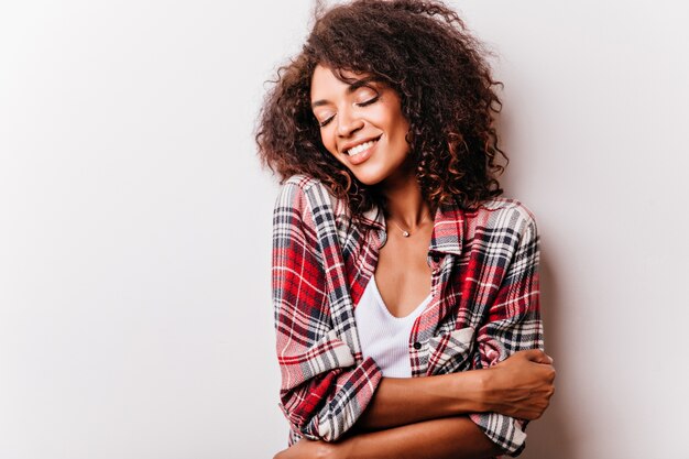 colpo di sensuale giovane donna africana. Incredibile ragazza bruna in camicia a scacchi rossa che ride con gli occhi chiusi.