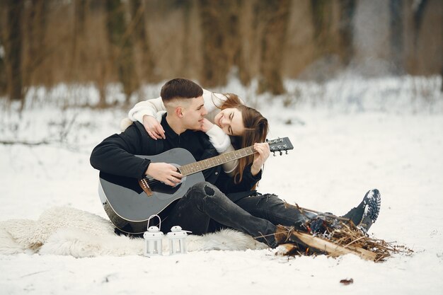 Colpo di stile di vita delle coppie che si siedono nella foresta nevosa. Persone che trascorrono le vacanze invernali all'aperto. Coppia con una chitarra.