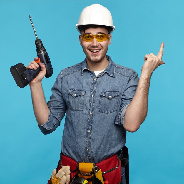 Colpo di studio isolato di allegro emotivo giovane riparatore indossando occhiali protettivi
