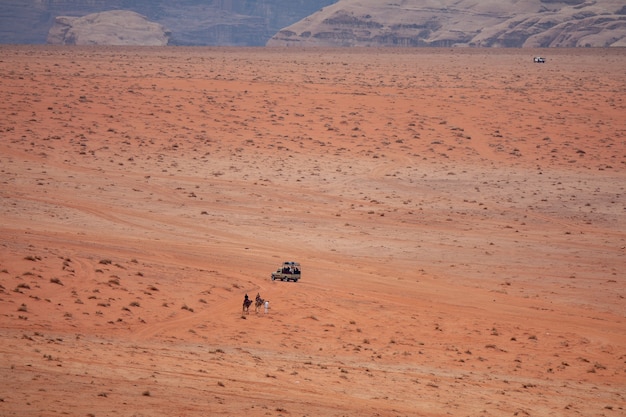 Colpo grandangolare di due persone sui cammelli che si avvicinano a un'auto in un deserto