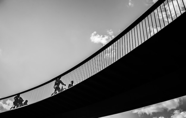 Colpo in scala di grigi di persone che vanno in bicicletta sul ponte
