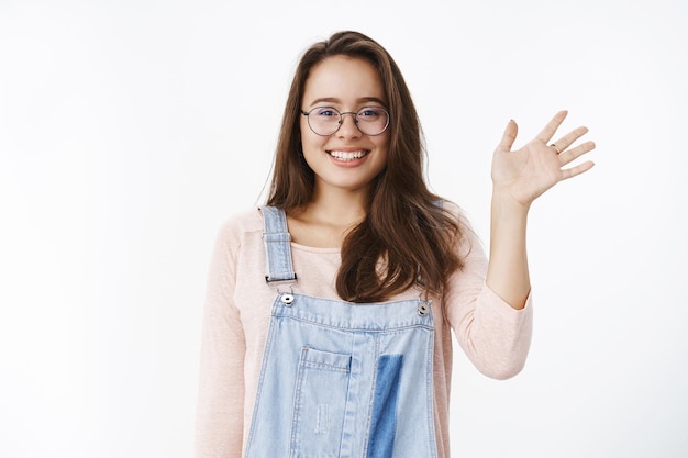 Colpo in vita di una simpatica ragazza principiante che saluta con speranza un nuovo collega, facendo amici sorridenti amichevoli e felici alla telecamera mentre alza il palmo in un gesto di saluto