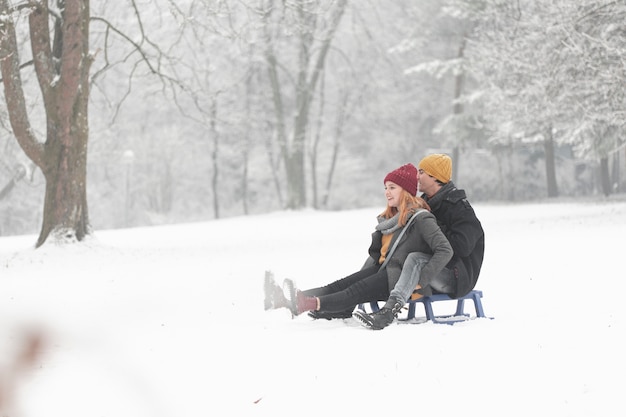 Colpo lungo delle coppie che giocano con la slitta nella neve